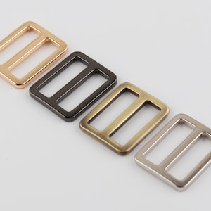 May include: Four metal slider buckles in different finishes: gold, black, brass, and silver.