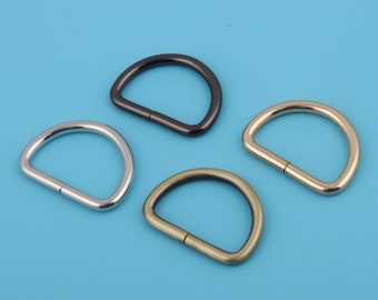 May include: Four metal D-rings in different finishes: silver, black, gold, and antique brass. The rings are all the same size and shape.