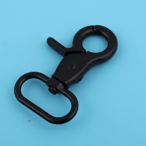 May include: Black metal swivel hook with a D-ring. The hook is designed to attach to a belt loop or other item.