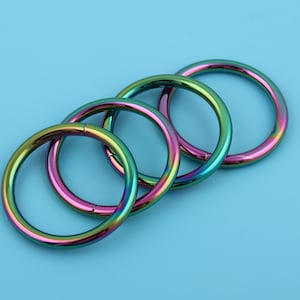 Puede incluir: Cuatro anillos de metal iridiscente, apilados uno encima del otro, con un acabado arcoíris. Los anillos son todos del mismo tamaño y están hechos de un metal duradero.