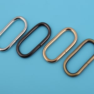 May include: Four oval-shaped metal rings in different finishes: silver, black, gold, and bronze. The rings are arranged in a row from left to right.