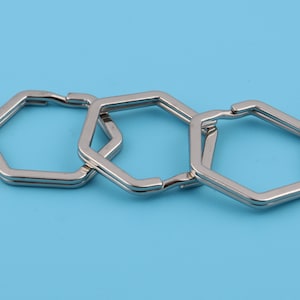 Könnte beinhalten: Drei silberne sechseckige Schlüsselringe, die miteinander verbunden sind. Die Ringe sind glatt und glänzend.