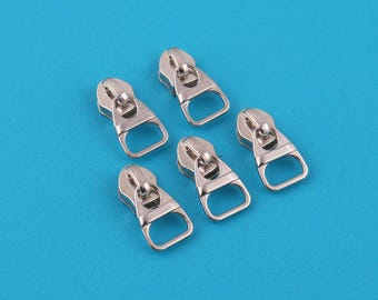 May include: Five silver-colored zipper pulls with a D-ring design are arranged on a bright blue surface. The zipper pulls are made of metal and have a shiny finish. These are likely for use in sewing or crafting projects.