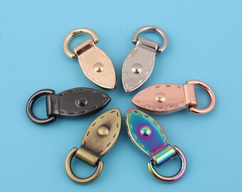 May include: Five different metal oval-shaped bag or purse hardware pieces with a ring on one end. The hardware pieces are in silver, gold, black, rose gold, and rainbow colors.