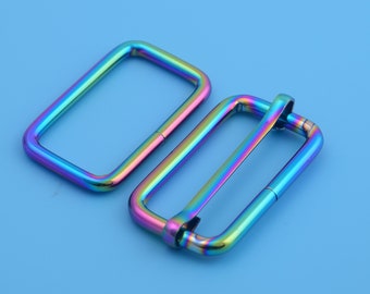 Op de afbeelding: Twee regenboogkleurige rechthoekige metalen gespen. De gespen zijn in een regenboog van kleuren, waaronder blauw, groen, paars en rood.