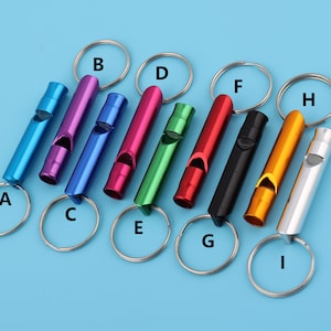 Puede incluir: Nueve silbatos de metal de diferentes colores con llaveros. Los silbatos son azules, morados, rojos, verdes, negros, naranjas, plateados y dorados. Los llaveros son plateados.