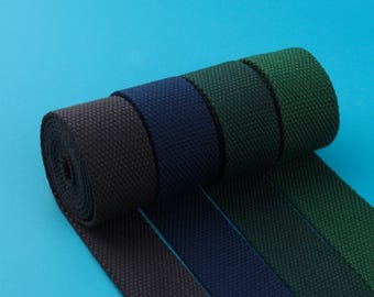 May include: A roll of woven fabric in shades of black, navy, green, and dark green. The fabric is tightly woven with a textured surface. The background is a solid light blue.