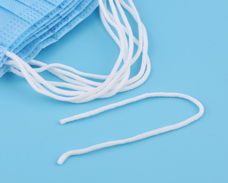 Op de afbeelding: Een close-up van witte elastische oorlussen voor gezichtsmaskers. De lussen zijn gemaakt van een zacht, rekbaar materiaal en zijn ontworpen om comfortabel over de oren te passen.