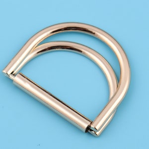 May include: A silver-toned metal D-ring with a double loop design. The ring is smooth and polished.
