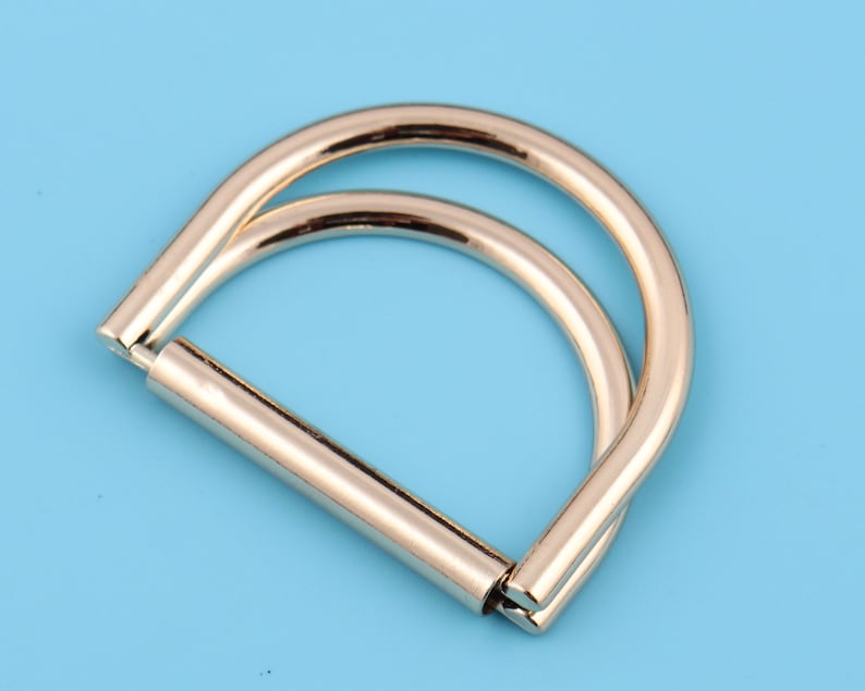May include: A silver-toned metal D-ring with a double loop design. The ring is smooth and polished.