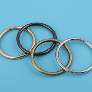 Puede incluir: Cuatro anillos metálicos de diferentes tamaños y acabados: dorado, negro, bronce y plateado. Los anillos están apilados uno encima del otro.