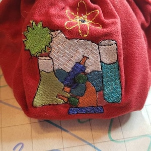 May include: Red drawstring bag with an embroidered design of a microscope, beakers, and an atom. The design is in shades of green, blue, orange, and white.