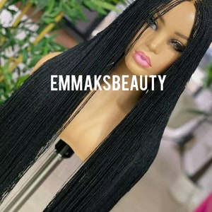 May include: Black micro braid wig with long, straight strands. The wig is on a mannequin head and the text "EMMAKSBEAUTY" is visible on the front of the wig.