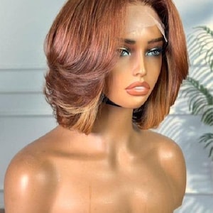 Op de afbeelding: Een kort, gelaagd pruik met een scheiding aan de zijkant. De pruik is een mix van lichtbruin en blond haar. De pruik is gestyled met losse golven en wordt gedragen op een mannequinhoofd.