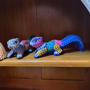 May include: Two hand-painted ceramic animal figurines. One is a blue squirrel with yellow, pink, and green details. The other is a gray and white animal with black spots.
