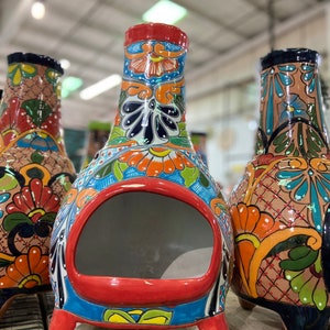 May include: Three colorful ceramic fire pits with intricate floral designs. The fire pits have a round opening and three legs. The designs feature bright colors like red, orange, yellow, blue, green, and black.