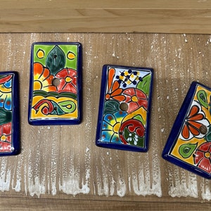 May include: Four colorful ceramic wall plates with a floral design. Each plate has a blue border and a hole in the center. The plates are arranged in a row on a wooden surface.
