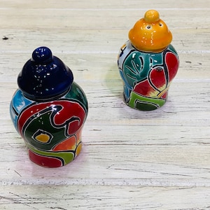 May include: Two colorful ceramic salt and pepper shakers with intricate floral designs. The shakers are hand-painted with vibrant colors, including blue, green, red, yellow, and orange.