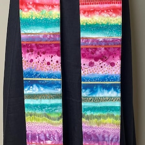 May include: A long, rectangular liturgical stole featuring a vibrant, multi-colored pattern of horizontal bands. The design includes watercolor-style washes, stippled dots, and fine vertical lines in shades of magenta, teal, lime green, and blue.