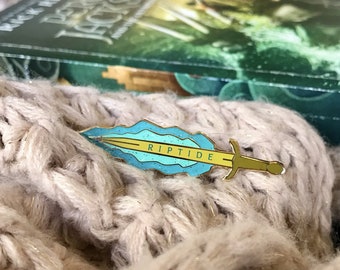 May include: A blue and gold enamel pin shaped like a sword with the word "RIPTIDE" on the blade.