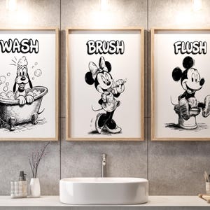May include: Three framed black and white Disney-themed bathroom art prints. The prints feature Pluto in a bathtub with the word "WASH", Minnie Mouse brushing her teeth with the word "BRUSH", and Mickey Mouse on the toilet with the word "FLUSH".