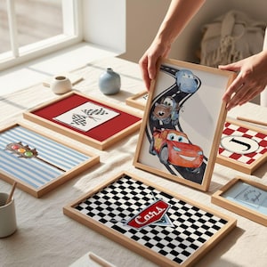 May include: A collection of framed art prints with a racing theme. One print features the word "Cars" on a checkered flag design. Other prints include a checkered flag, a traffic light, and a race car illustration. The frames are made of light-colored wood.