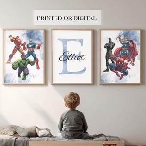 May include: Three framed prints with superhero illustrations and a personalised initial. The superhero prints feature Iron Man, Captain America, Hulk, Black Panther, Thor, and Spider-Man. The third print displays a blue letter "E" with the name "Elliot". The text "PRINTED OR DIGITAL" is at the top.