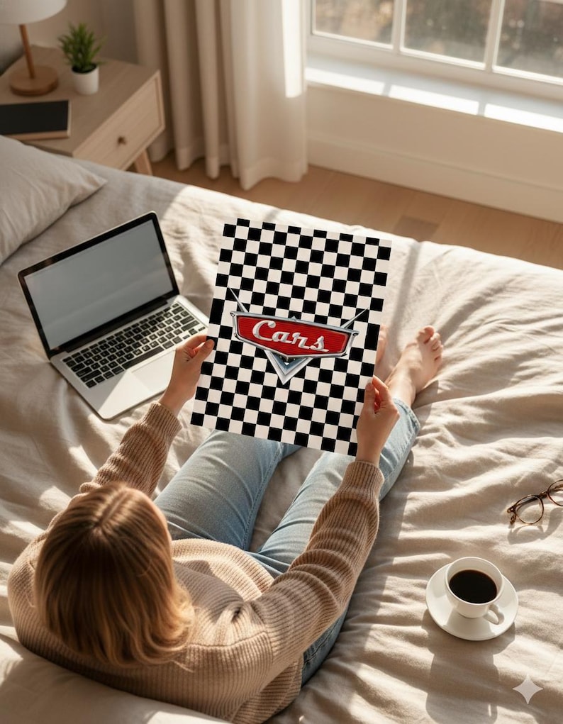 May include: A person holding a poster with a black and white checkered pattern and the word "Cars" in red and white. The poster is held over a bed with a laptop, coffee, and glasses nearby.