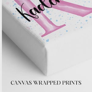 K&ouml;nnte beinhalten: Eine Leinwanddruck mit dem Namen "Kadence" in schwarzer Schrift &uuml;ber einem gro&szlig;en rosa Buchstaben "K". Der Hintergrund hat blaue und rosa Farbspritzer. Der Text "CANVAS WRAPPED PRINTS" steht unten.