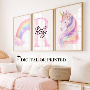 May include: Three framed art prints featuring a rainbow, a pink letter 'R' with the name 'Riley', and a unicorn. The prints have gold frames and are displayed above a bed with pink bedding. The text 'DIGITAL OR PRINTED' is at the bottom.