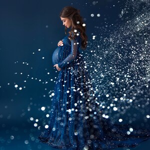 May include: A pregnant woman in a blue sparkly gown stands in front of a dark blue background with silver glitter falling around her.