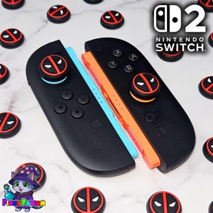 May include: Black Nintendo Switch Joy-Con controllers with Deadpool-themed thumb grips. The controllers have a blue and orange centre. The image also includes additional Deadpool thumb grips and the Nintendo Switch logo.