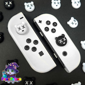 May include: White Nintendo Switch Joy-Con controllers with black buttons and bear-shaped thumb grips. The bear grips have an "XX" design. Additional bear-shaped grips are scattered around the controllers. The Pixel Potion logo is visible in the bottom left corner.