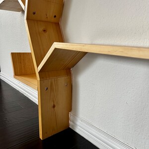 Op de afbeelding: Een zeshoekige houten plank met meerdere planken. De plank is gemaakt van natuurlijk hout en heeft een lichtbruine afwerking. De planken zijn schuin en cre&euml;ren een uniek geometrisch ontwerp.