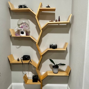 Op de afbeelding: Een houten boomvormig rek met meerdere planken. De planken zijn gevuld met verschillende items, waaronder een glazen koepel met bloemen, camera's en kleine beeldjes.