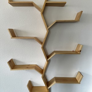 Op de afbeelding: Een houten wandplank met een uniek boomtakontwerp. De plank heeft vijf planken, elk met een andere vorm en grootte. De planken zijn gemaakt van natuurlijk hout en hebben een lichtbruine afwerking.