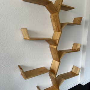 Op de afbeelding: Een houten wandplank met een uniek boomvormig ontwerp. De plank heeft zes planken die schuin zijn geplaatst en met elkaar verbonden zijn om een vertakkingseffect te cre&euml;ren. De plank is gemaakt van natuurlijk hout en heeft een lichtbruine afwerking.