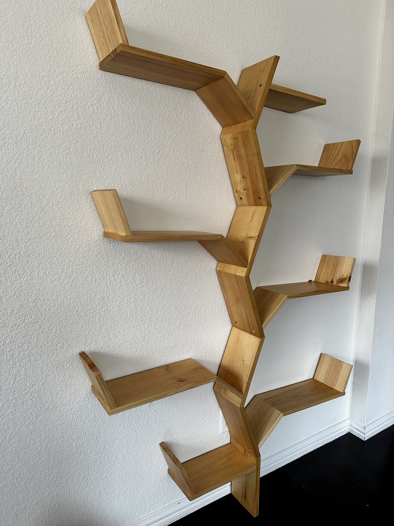 Op de afbeelding: Een houten wandplank met een uniek boomvormig ontwerp. De plank heeft zes planken die schuin zijn geplaatst en met elkaar verbonden zijn om een vertakkingseffect te cre&euml;ren. De plank is gemaakt van natuurlijk hout en heeft een lichtbruine afwerking.