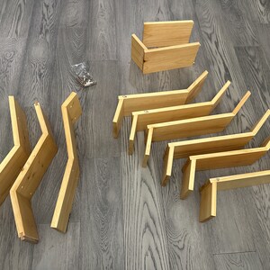 Op de afbeelding: Een set onafgewerkte houten plankensteunen, klaar om te beitsen of te schilderen. De steunen zijn in verschillende maten en vormen, sommige met een gebogen ontwerp.