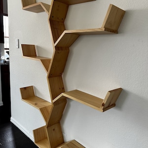 Op de afbeelding: Een houten wandplank in de vorm van een boom met meerdere takken en planken. De planken zijn gemaakt van natuurlijk hout en hebben een lichtbruine afwerking.