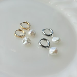 May include: Two pairs of hoop earrings with a pearl drop. One pair has gold hoops, the other has silver hoops. The pearls are white and irregularly shaped. The earrings are displayed on a white surface.