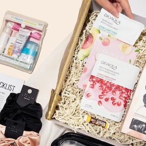 May include: A gift box filled with beauty and self-care items. Includes face masks, spa gel socks, lip balm, and a travel essentials kit. A hospital bag checklist and scrunchies are also visible.