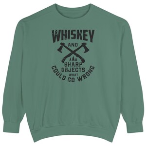May include: Green sweatshirt featuring the text "Whiskey and Sharp Objects, What Could Go Wrong" in black. The design includes crossed axes and a mountain graphic.