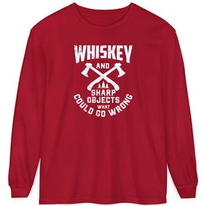 May include: A long-sleeved red shirt with a white graphic. The graphic reads "Whiskey and Sharp Objects, What Could Go Wrong" with crossed axes. The shirt is made of a soft material.