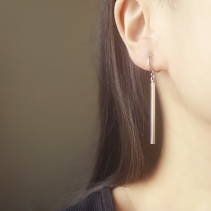May include: A silver bar earring with a hoop at the top. The earring is hanging from a person's ear.