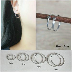 Peut inclure: Boucles d'oreilles créoles argentées de différentes tailles, de 2 cm à 5 cm. Une boucle d'oreille est portée, tandis que d'autres sont présentées sur une baguette en bois. L'image comprend une étiquette de taille de 2 cm.