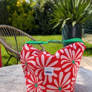 Pode incluir: Saco de almoço vermelho e branco com padrão floral, com alça e fecho de fivela verdes. O saco tem formato retangular e uma pequena etiqueta branca com o texto "BINOUX".