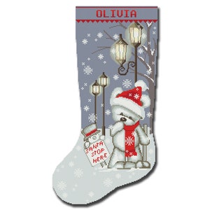 Könnte beinhalten: Ein grauer Weihnachtssocken mit einem weißen Teddybär, der einen roten Weihnachtsmann-Hut und einen Schal trägt und vor einer Straßenlaterne steht. Der Socken hat einen weißen Hintergrund mit Schneeflocken und den Namen "Olivia" oben.