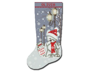 May include: A gray Christmas stocking with a white teddy bear wearing a red Santa hat and scarf standing in front of a streetlight. The stocking has a white background with snowflakes and the name "Olivia" at the top.