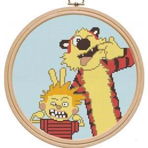 May include: A cross-stitch embroidery of a cartoon tiger and a boy with a red and white striped shirt. The tiger is yellow with black stripes and a red scarf. The boy has orange hair and is making a peace sign with his fingers.